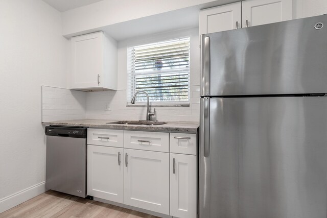 kitchen featuring white cabinets, sink, light stone countertops, appliances with stainless steel finishes, and light hardwood / wood-style floors