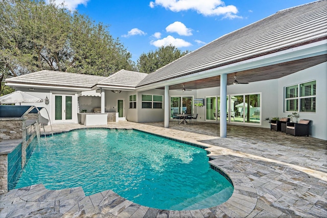 view of pool featuring french doors, an outdoor kitchen, pool water feature, ceiling fan, and a patio area