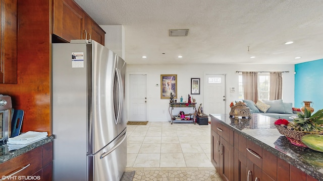 kitchen with light tile patterned floors, stainless steel refrigerator, dark stone countertops, and a textured ceiling