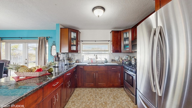 kitchen featuring a textured ceiling, appliances with stainless steel finishes, dark stone counters, a healthy amount of sunlight, and sink