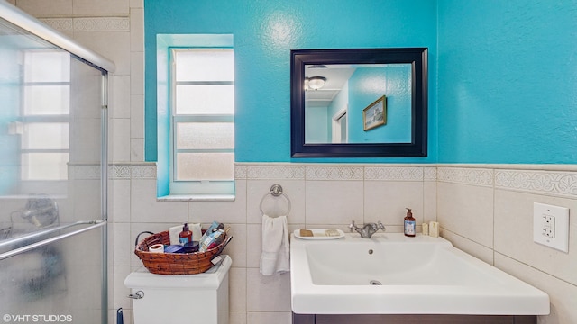 bathroom with toilet, tile walls, a shower with door, and sink