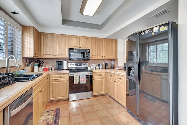 kitchen featuring backsplash, a raised ceiling, sink, black appliances, and tile countertops