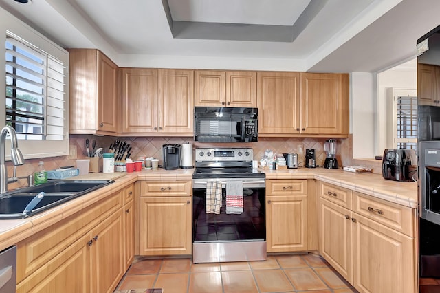 kitchen featuring backsplash, sink, a tray ceiling, tile counters, and stainless steel appliances