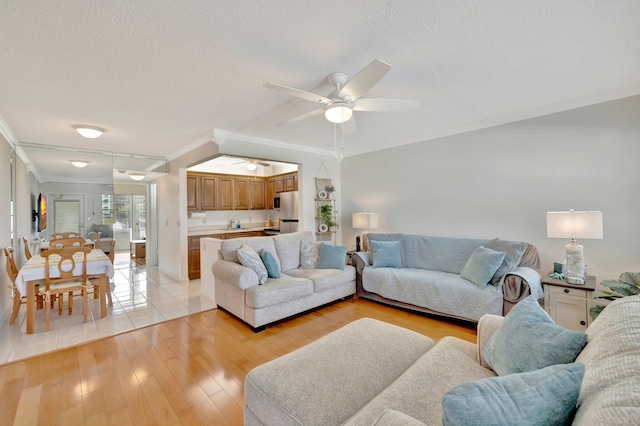 living room featuring ceiling fan, light hardwood / wood-style floors, a textured ceiling, and ornamental molding