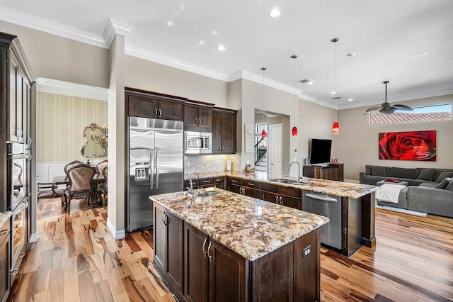 kitchen with a kitchen island with sink, hanging light fixtures, built in appliances, ceiling fan, and ornamental molding