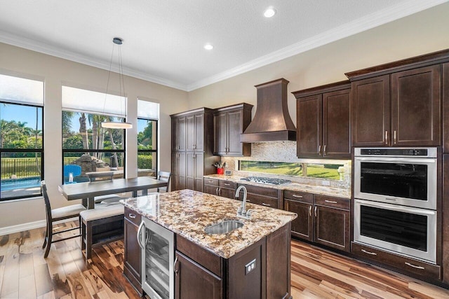 kitchen featuring backsplash, premium range hood, beverage cooler, sink, and pendant lighting