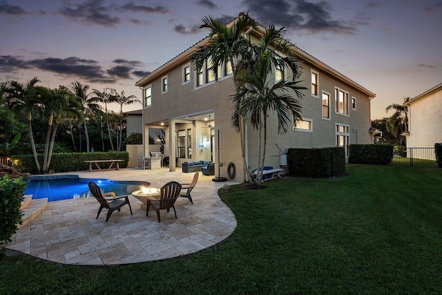 back house at dusk with an outdoor living space with a fire pit, exterior kitchen, a patio area, a fenced in pool, and a lawn