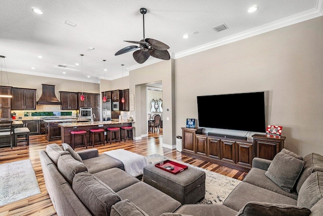 living room featuring a textured ceiling, light hardwood / wood-style floors, ceiling fan, and crown molding