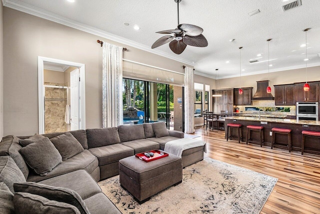 living room featuring a textured ceiling, light hardwood / wood-style floors, ceiling fan, and ornamental molding