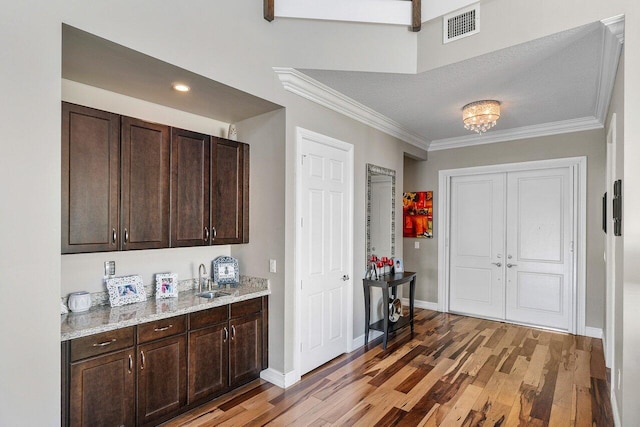 bar with light stone countertops, ornamental molding, dark brown cabinetry, sink, and wood-type flooring