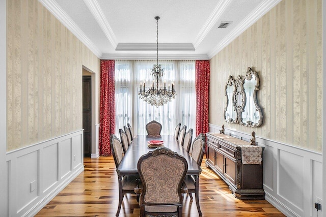 dining room with a chandelier, light hardwood / wood-style flooring, a raised ceiling, and ornamental molding