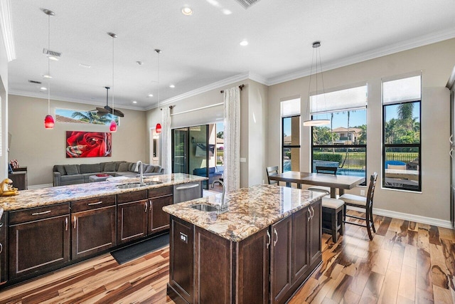 kitchen featuring decorative light fixtures, a center island with sink, light stone counters, and sink