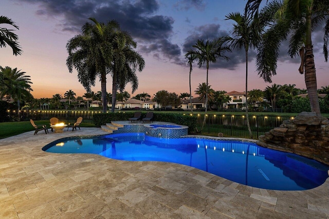 pool at dusk featuring an in ground hot tub, a patio, and an outdoor fire pit