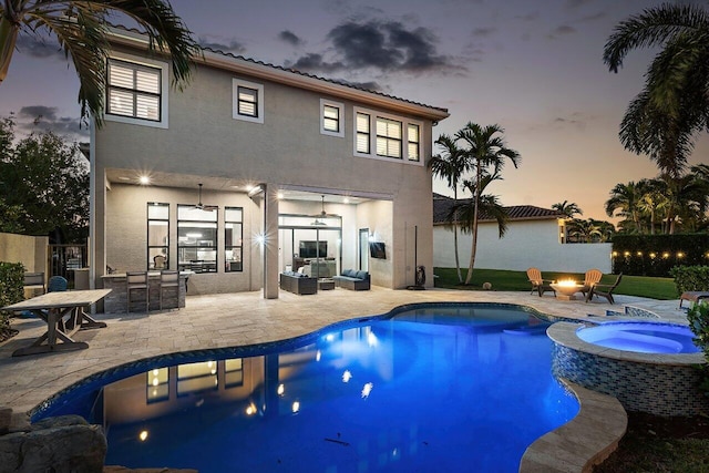 pool at dusk with an outdoor living space with a fire pit, an in ground hot tub, ceiling fan, and a patio