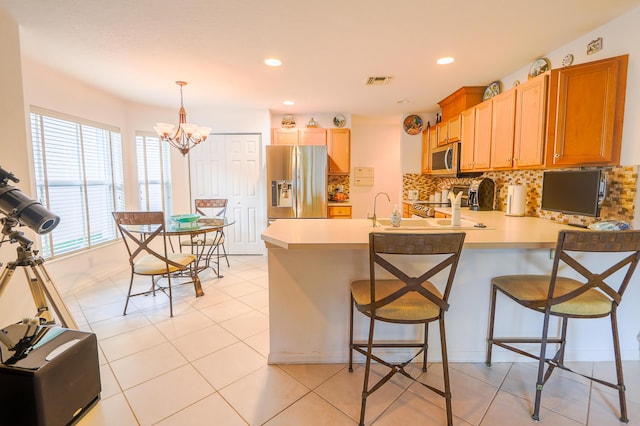 kitchen featuring stainless steel appliances, an inviting chandelier, pendant lighting, a kitchen bar, and light tile patterned floors