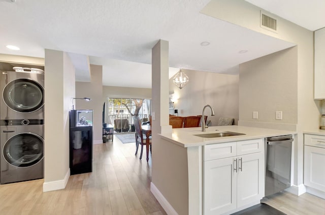 kitchen with stacked washer / drying machine, kitchen peninsula, stainless steel dishwasher, white cabinets, and sink