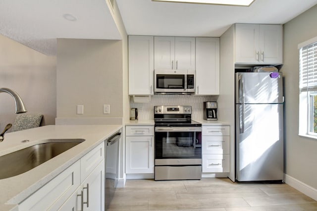 kitchen with appliances with stainless steel finishes, white cabinetry, sink, backsplash, and light wood-type flooring