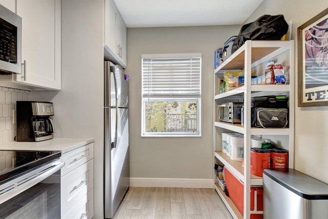 kitchen featuring white cabinetry, tasteful backsplash, light hardwood / wood-style floors, stainless steel fridge, and range with electric stovetop