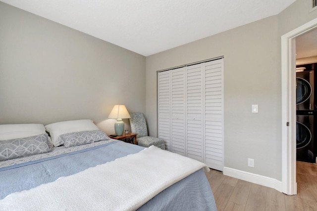 bedroom with light hardwood / wood-style floors, stacked washer / drying machine, and a closet