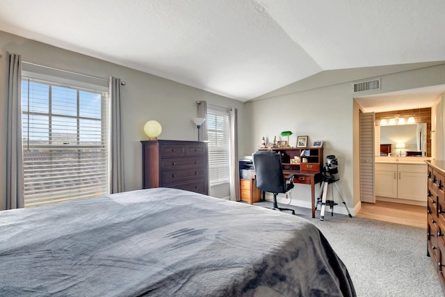 carpeted bedroom with ensuite bath, multiple windows, and lofted ceiling