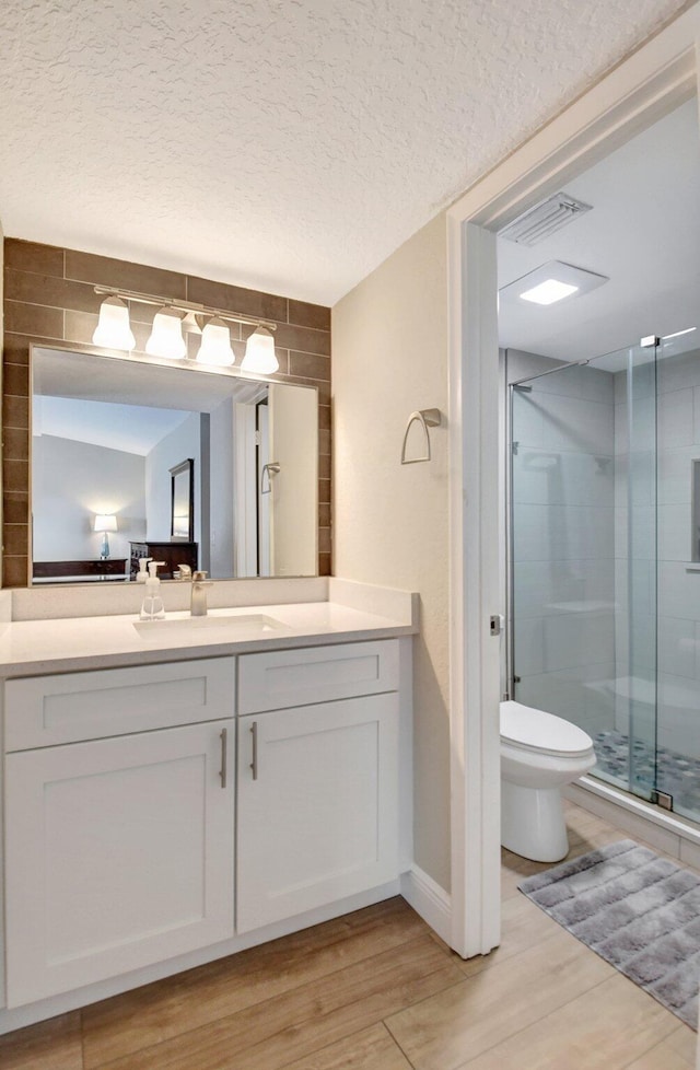 bathroom featuring toilet, a textured ceiling, a shower with shower door, and vanity