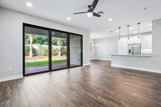 unfurnished living room with a textured ceiling, ceiling fan with notable chandelier, and dark wood-type flooring