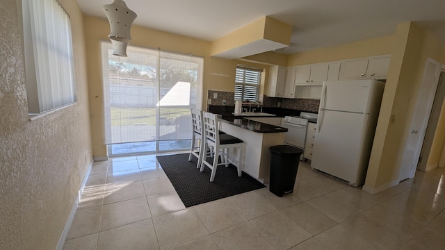 kitchen featuring white cabinetry, tasteful backsplash, white appliances, a breakfast bar, and light tile patterned floors