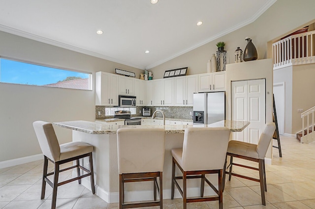 kitchen with appliances with stainless steel finishes, white cabinetry, ornamental molding, light stone counters, and a breakfast bar area