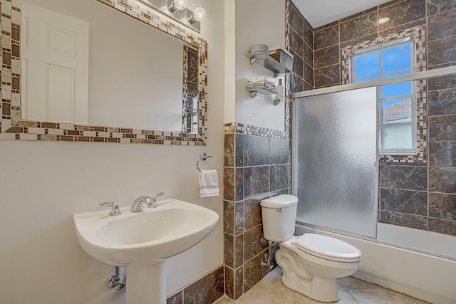 full bathroom with toilet, bath / shower combo with glass door, tile walls, tile patterned floors, and sink