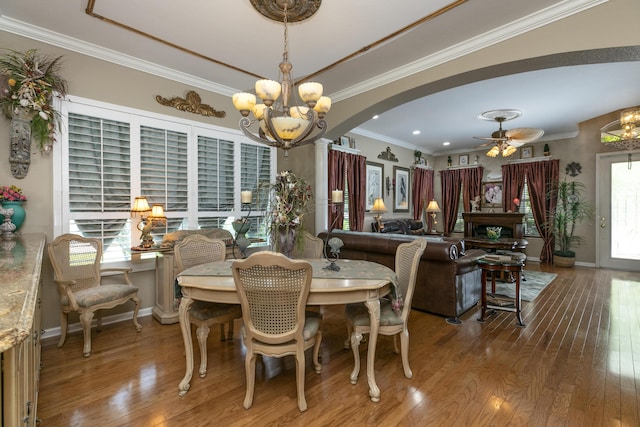 dining area with ceiling fan with notable chandelier, wood-type flooring, and crown molding