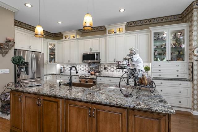 kitchen featuring pendant lighting, dark stone countertops, an island with sink, appliances with stainless steel finishes, and white cabinetry