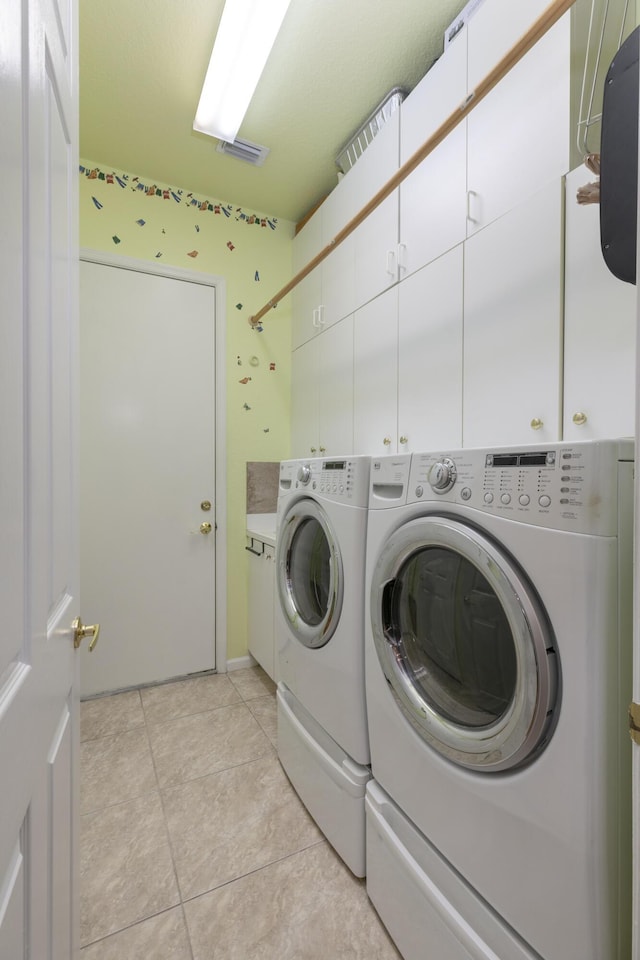 clothes washing area featuring washer and clothes dryer, light tile patterned floors, and cabinets