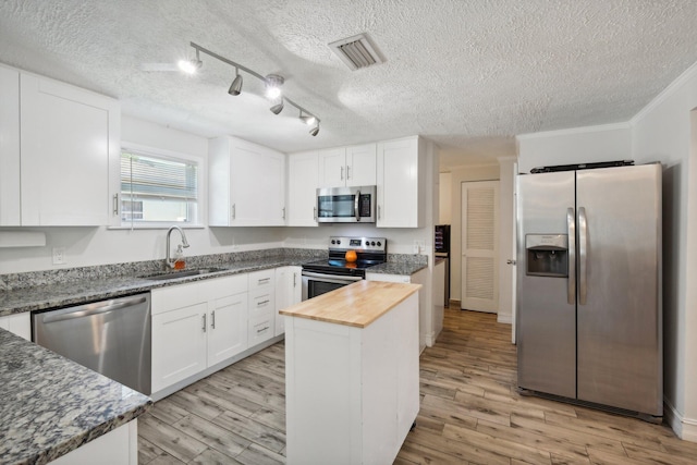 kitchen with sink, stainless steel appliances, a kitchen island, track lighting, and white cabinets