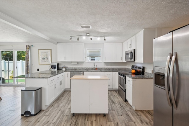 kitchen featuring white cabinets, appliances with stainless steel finishes, a kitchen island, and dark stone countertops