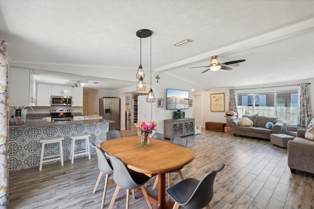 dining space with sink, light hardwood / wood-style flooring, vaulted ceiling with beams, ceiling fan, and a textured ceiling