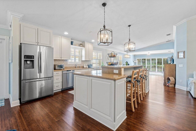 kitchen with decorative light fixtures, a kitchen island, white cabinetry, appliances with stainless steel finishes, and a kitchen breakfast bar