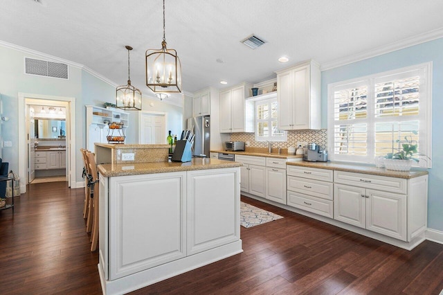 kitchen featuring white cabinets, appliances with stainless steel finishes, a kitchen island, dark wood-type flooring, and hanging light fixtures