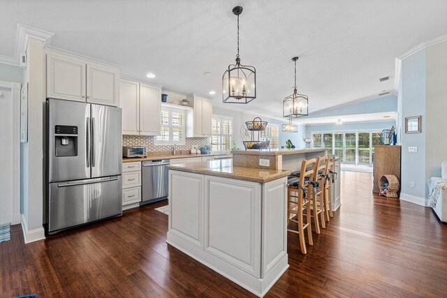 kitchen with lofted ceiling, pendant lighting, stainless steel dishwasher, sink, and white cabinets