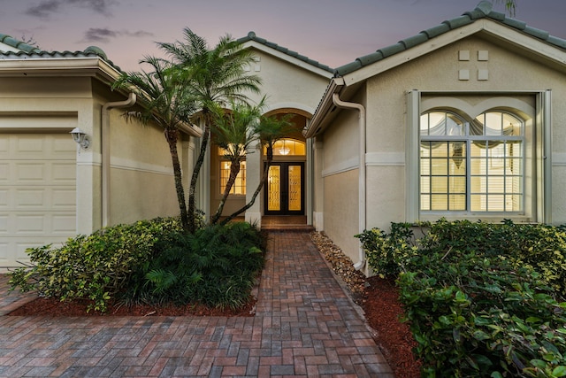 exterior entry at dusk featuring a garage and french doors