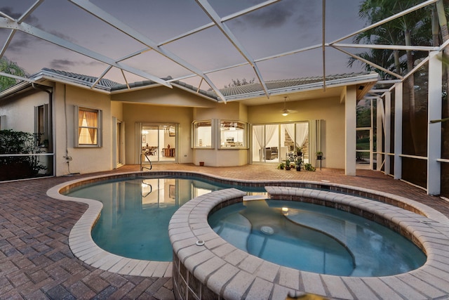 pool at dusk featuring a lanai, a patio, and an in ground hot tub