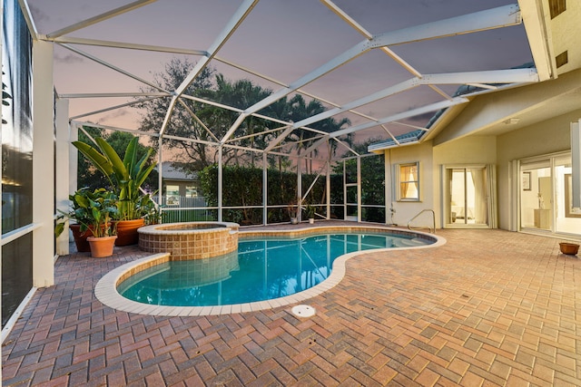 pool at dusk featuring an in ground hot tub, a patio, and glass enclosure