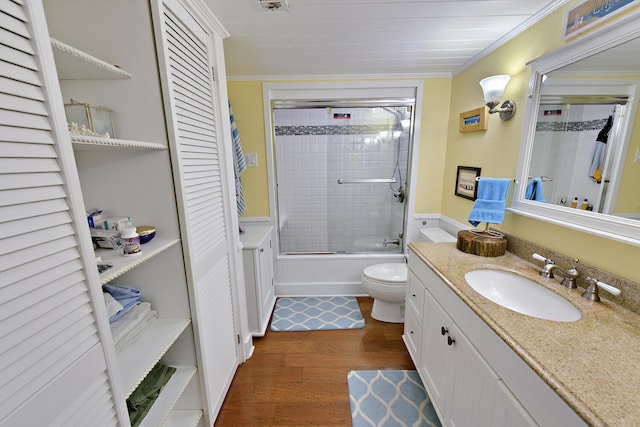 full bathroom featuring bath / shower combo with glass door, vanity, crown molding, hardwood / wood-style flooring, and toilet