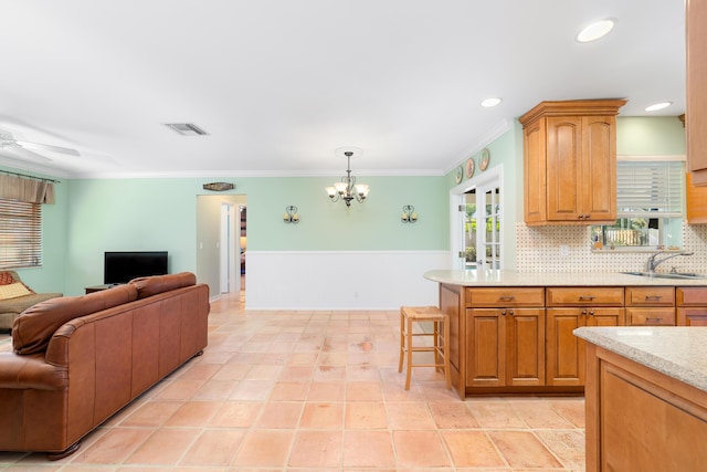 kitchen with ceiling fan with notable chandelier, pendant lighting, decorative backsplash, sink, and crown molding