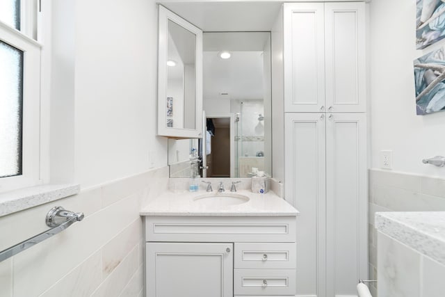 bathroom with a shower with shower door, vanity, tile walls, and a wealth of natural light