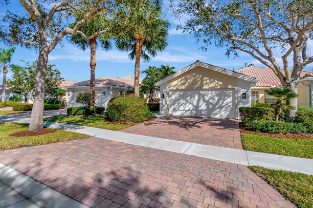 view of front of property featuring a garage, decorative driveway, a tiled roof, and stucco siding