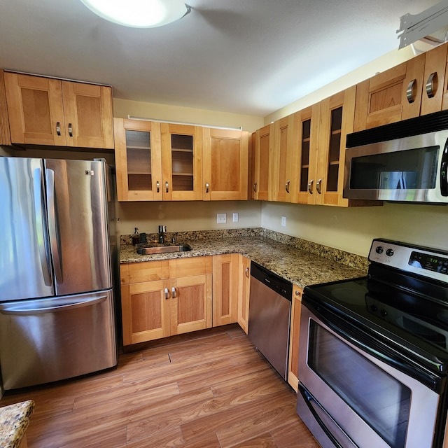 kitchen featuring sink, light hardwood / wood-style floors, dark stone counters, and appliances with stainless steel finishes