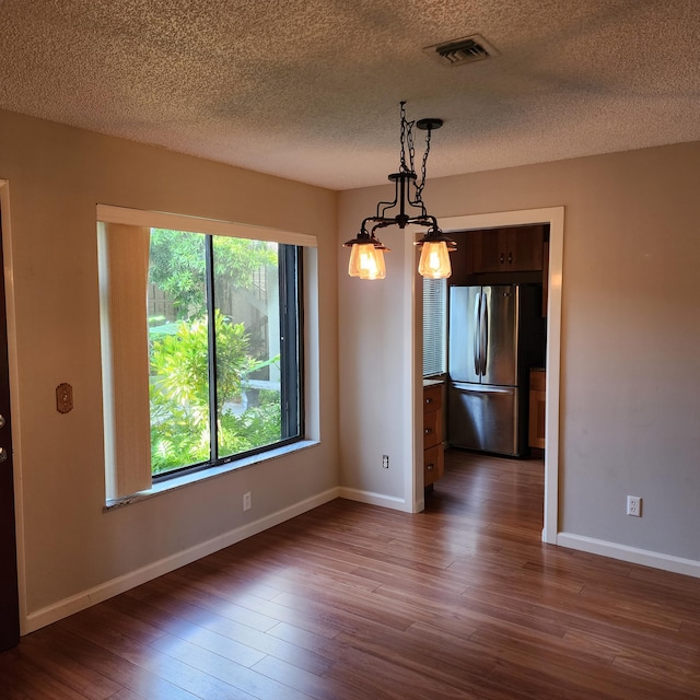 unfurnished dining area featuring dark wood-type flooring, an inviting chandelier, and a textured ceiling