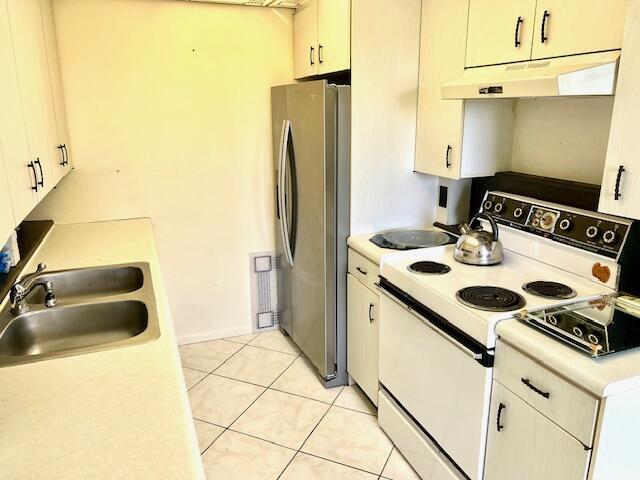 kitchen with white range with electric cooktop, light tile patterned floors, sink, and stainless steel refrigerator