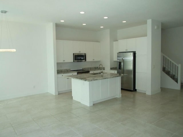 kitchen with appliances with stainless steel finishes, a kitchen island with sink, sink, white cabinets, and hanging light fixtures