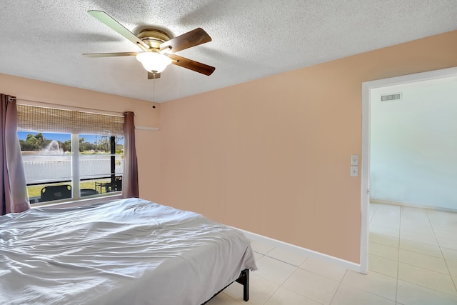 bedroom featuring ceiling fan, light tile patterned floors, and a textured ceiling